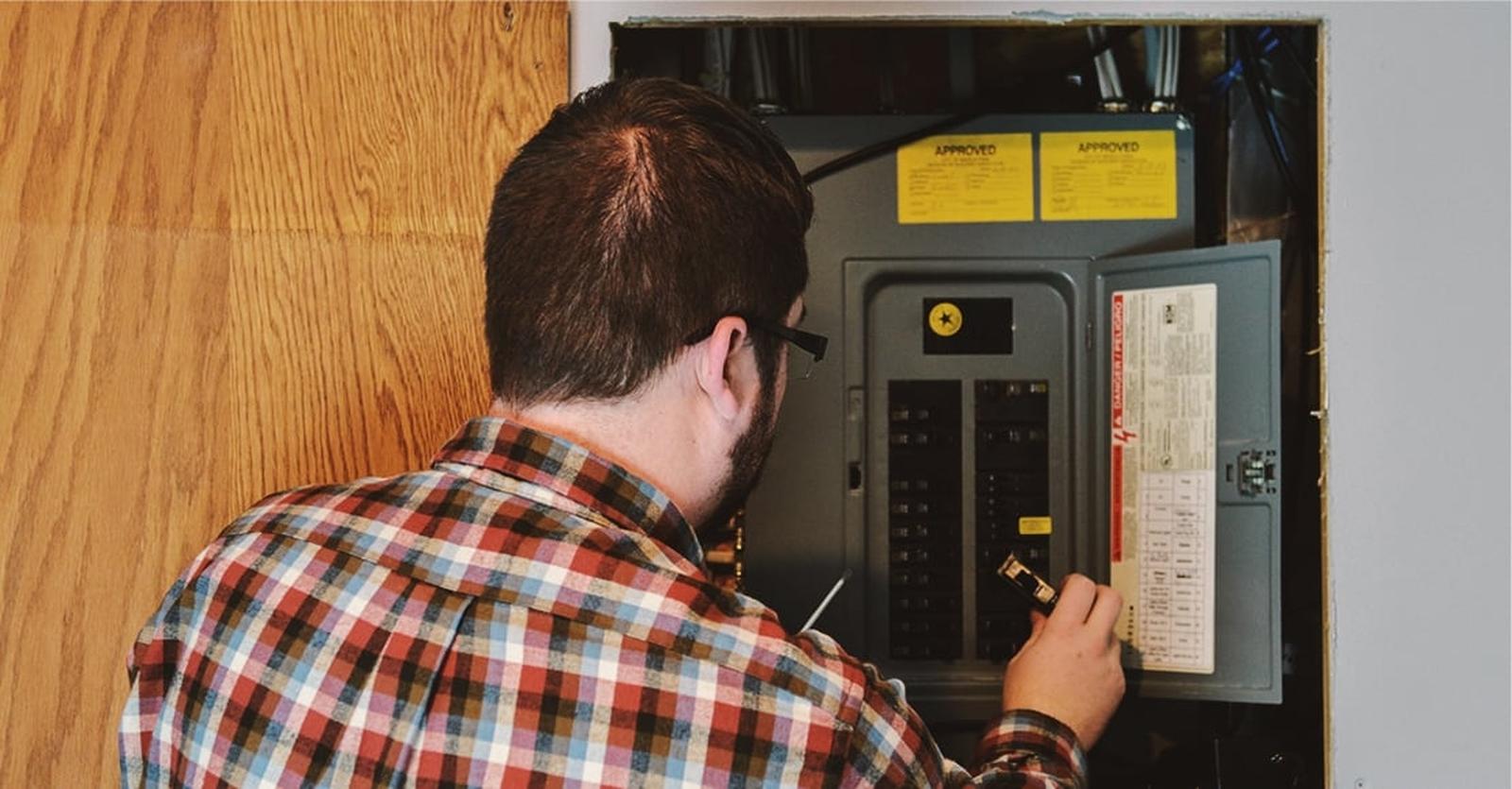 Person holding a breaker while standing near a main electrical breaker box.