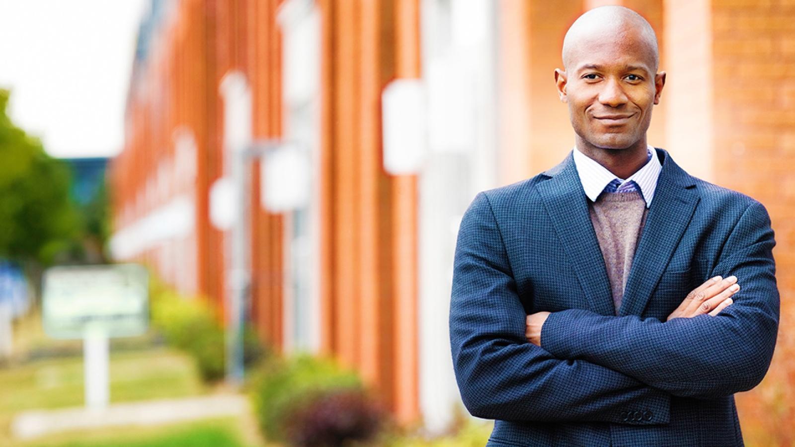Business professional smiling with arms crossed, standing in front of an apartment building.