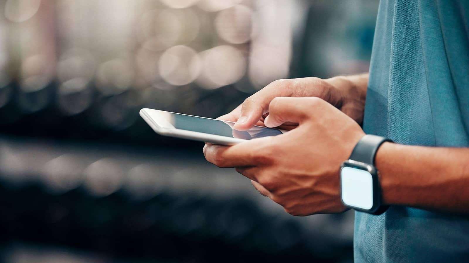 Person in a blue shirt using a smartphone, wearing a smartwatch, with a blurred background.