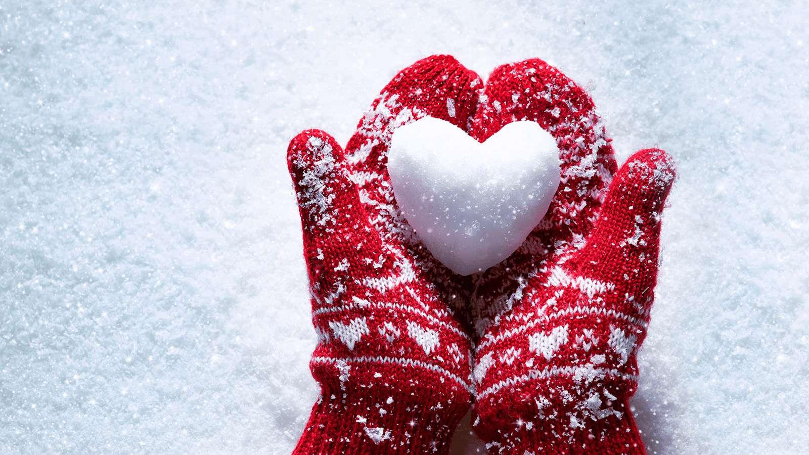 Two hands in red mittens hold snow shaped like a heart