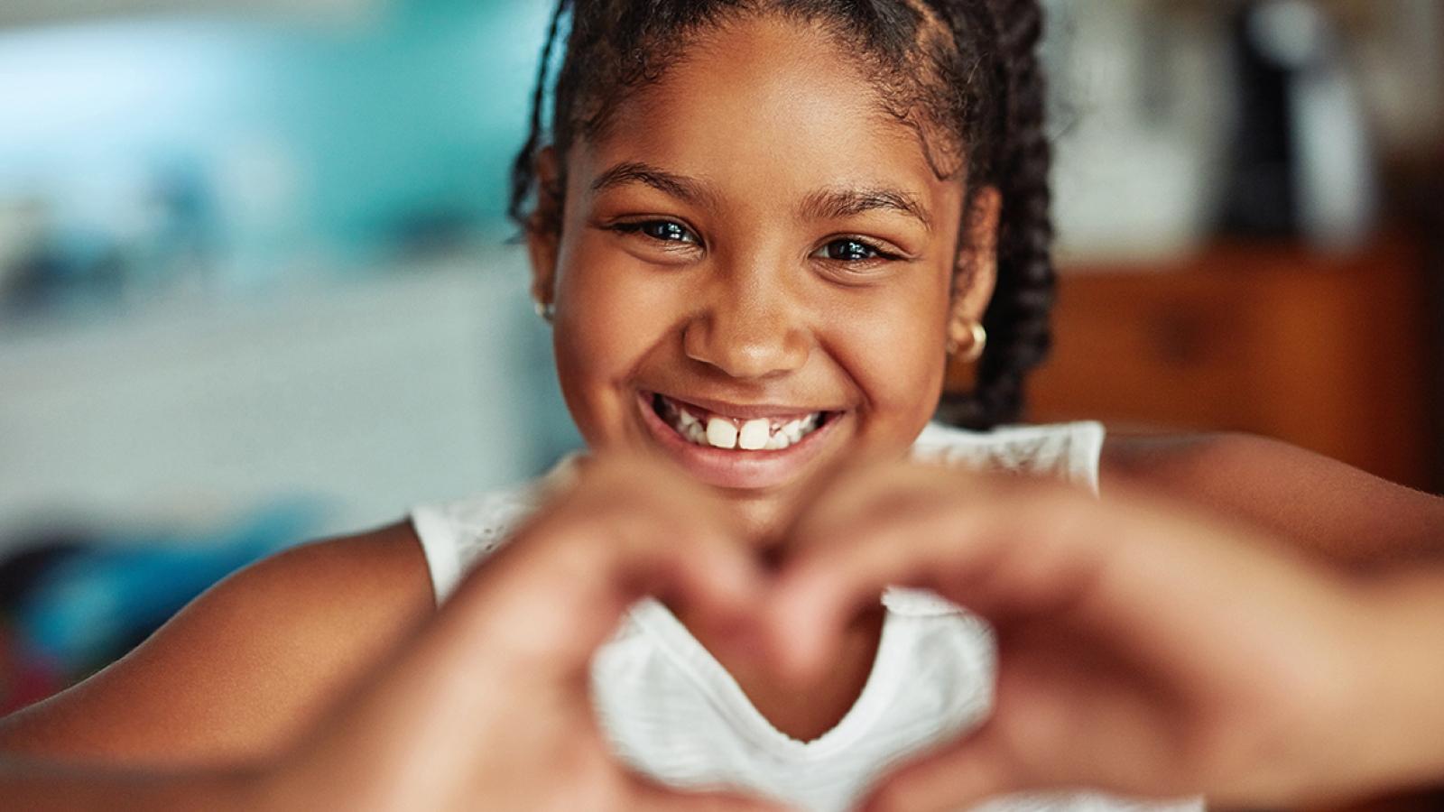 Young girl smiles and holds her hands in a heart shape