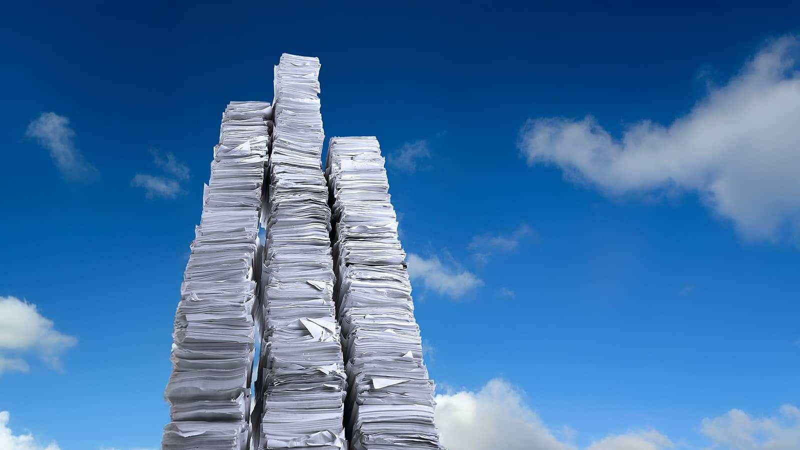 Three tall stacks of papers. The background is a sky with clouds.