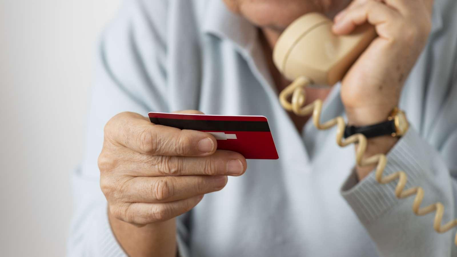 Person holding a credit card while talking on a landline phone.