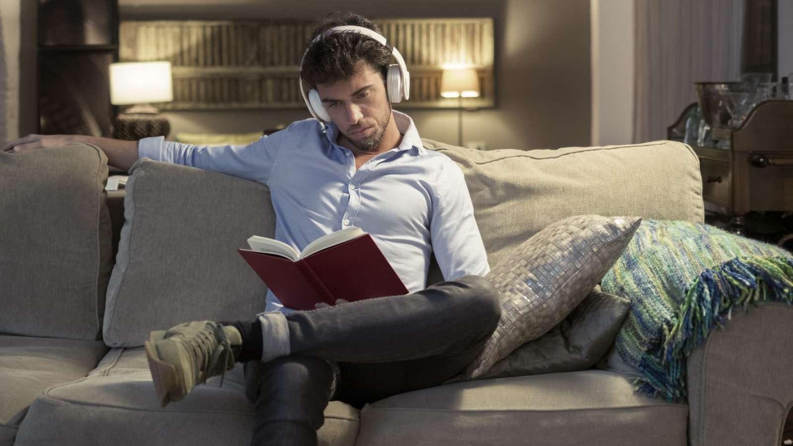 Person sitting on a couch with headphones on, reading a book