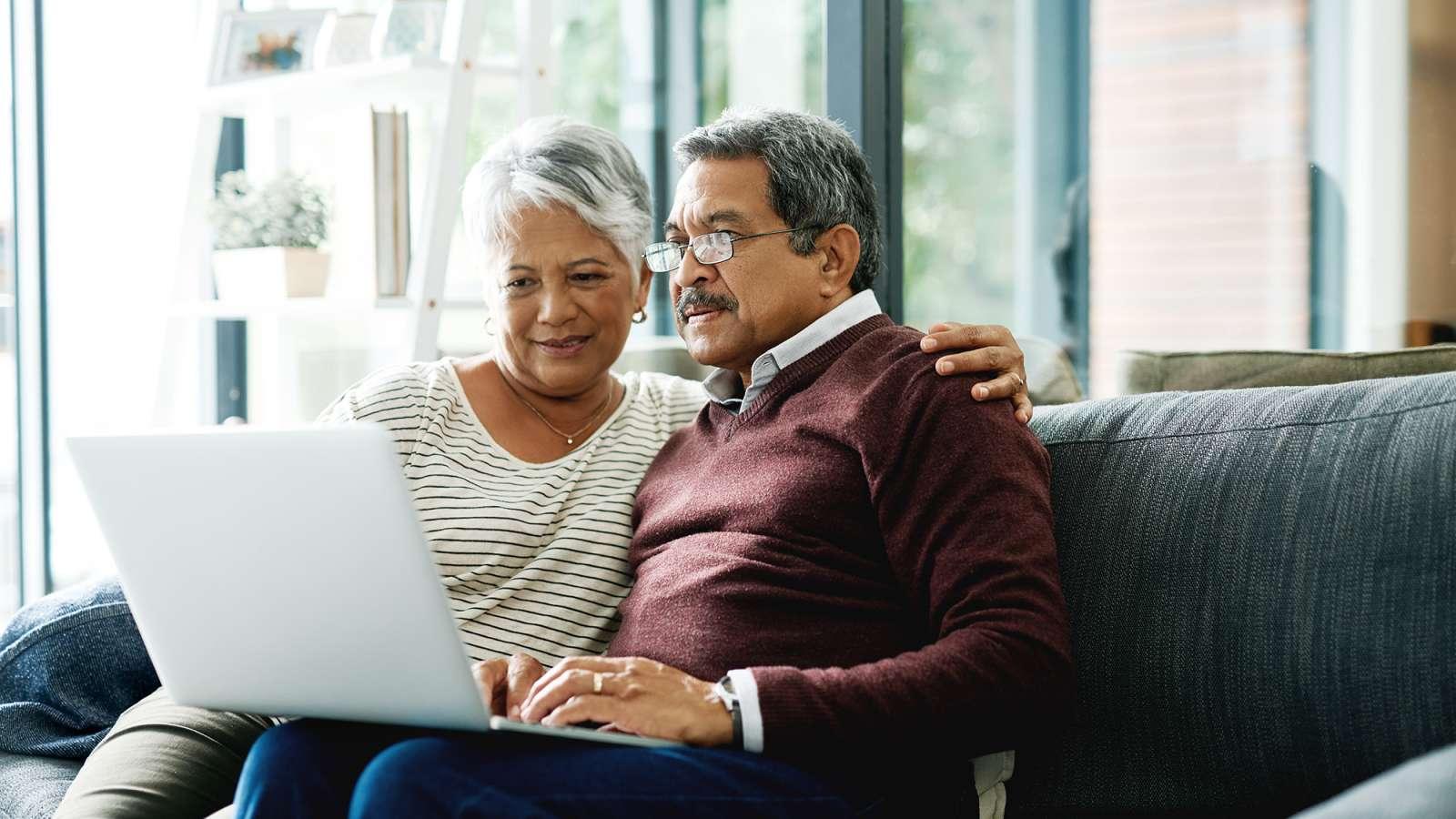 Couple sitting on a couch looking at a laptop.
