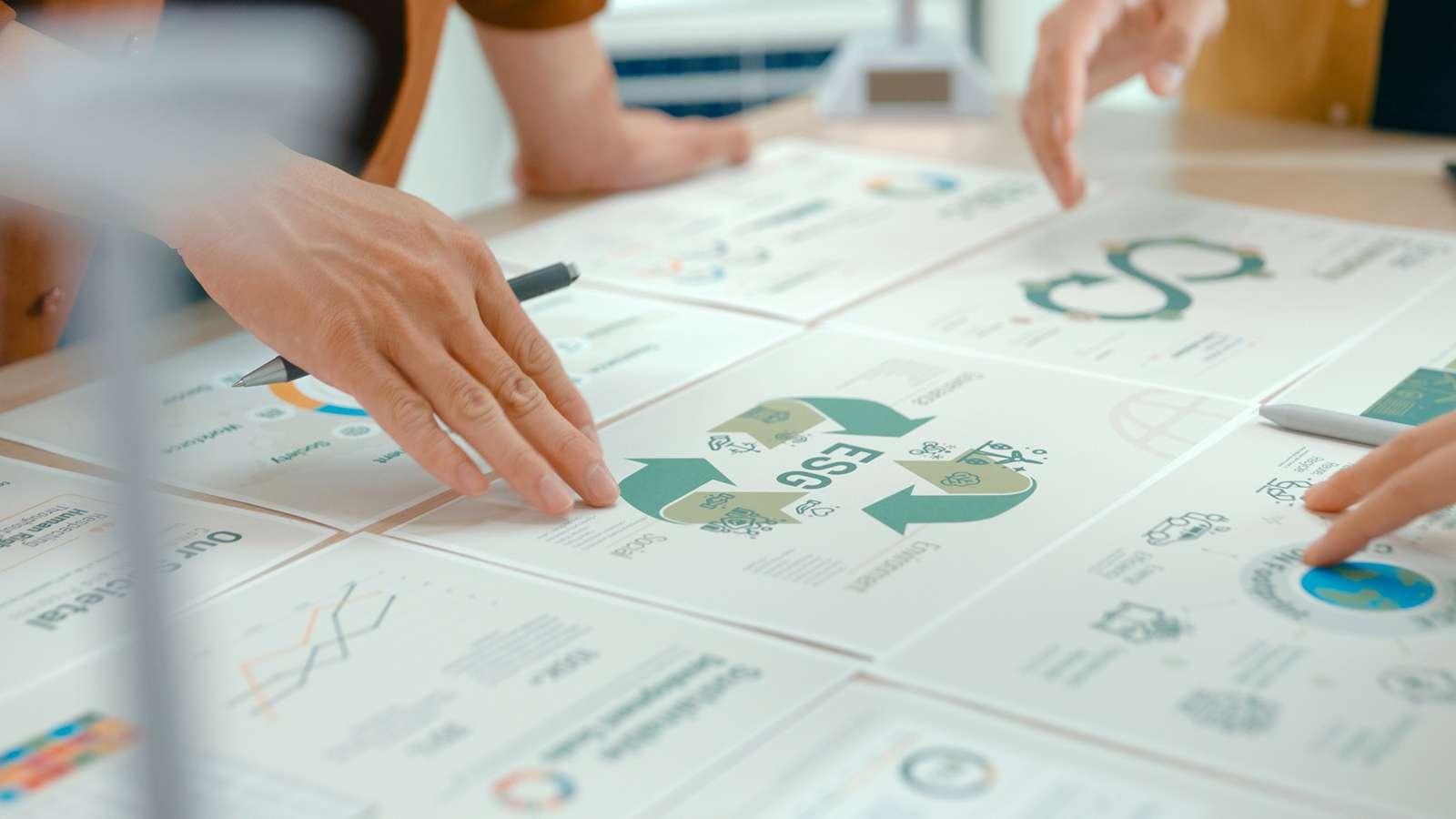 Hands pointing at ESG and sustainability charts, graphs, and diagrams on a table.