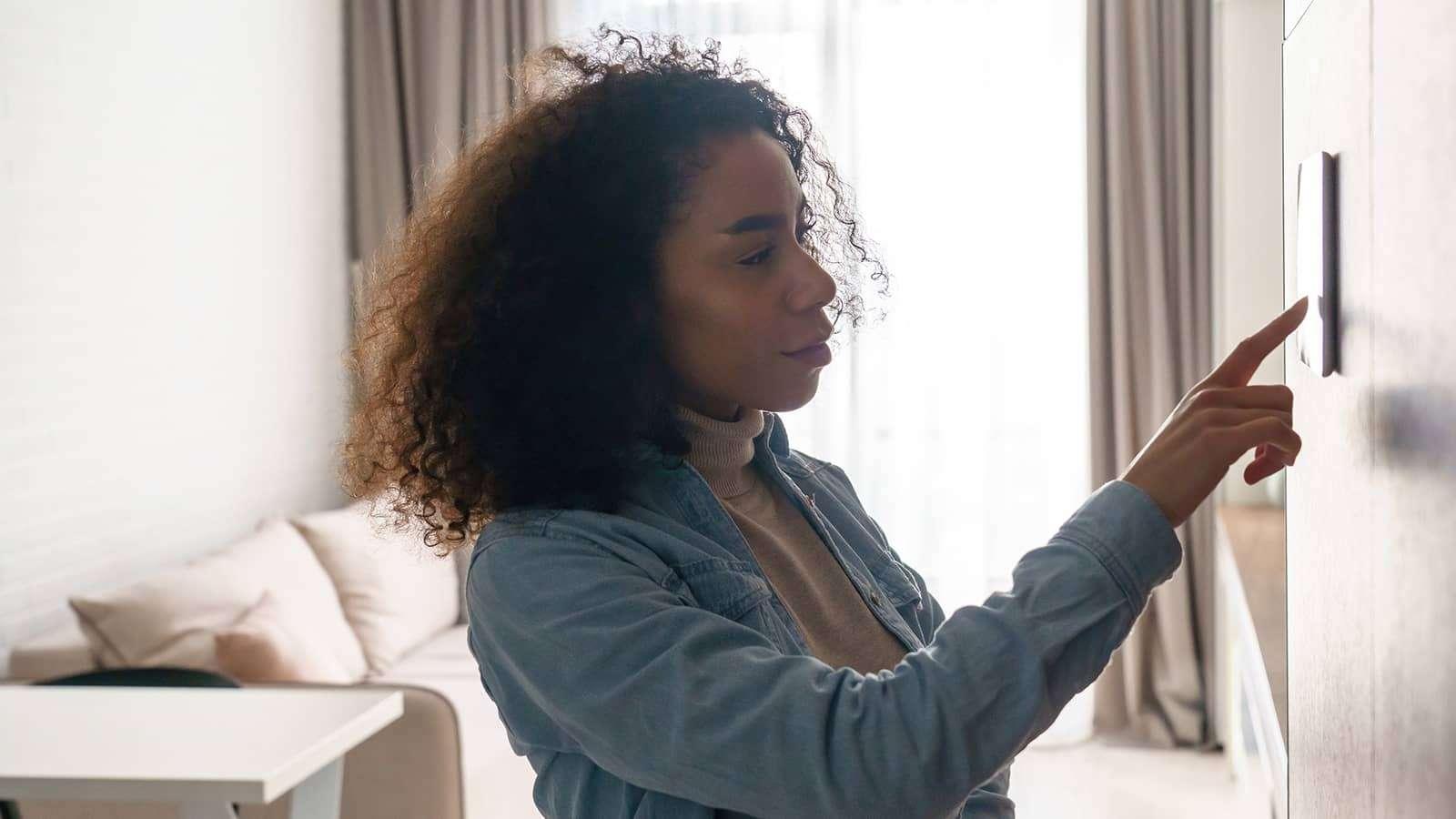 Woman operating a thermostat on the wall indoors