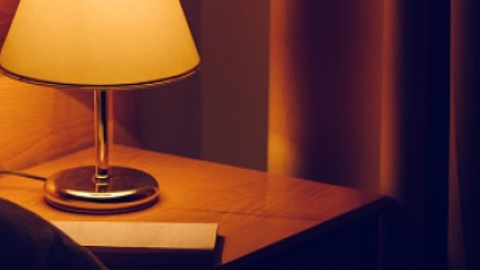 Lamp on a bedside table with a curtain in the background.