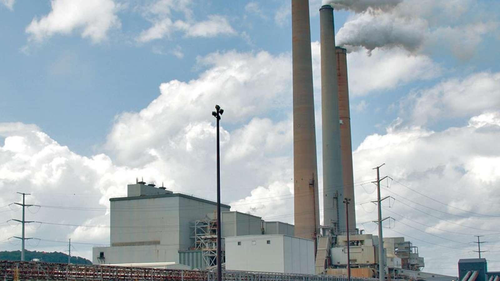 A power plant with tall chimneys under a partly cloudy sky, surrounded by utility poles and industrial structures.