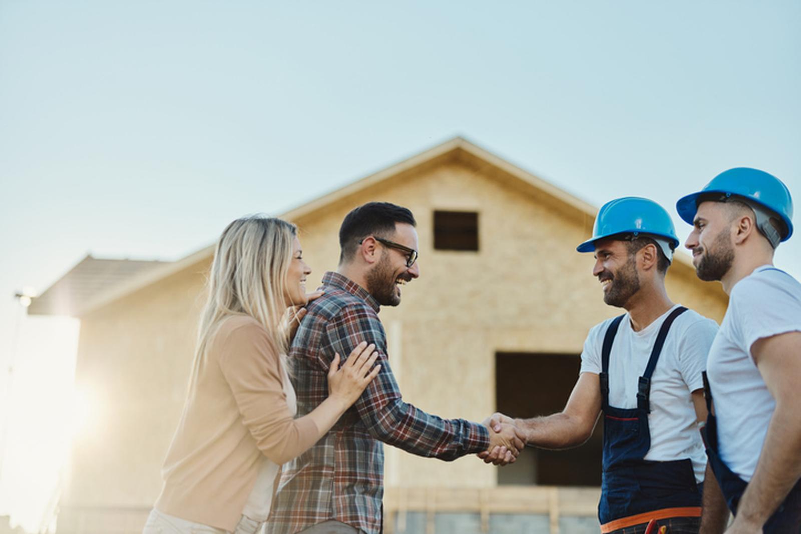 Couple shaking hands with construction workers in front of a house under construction